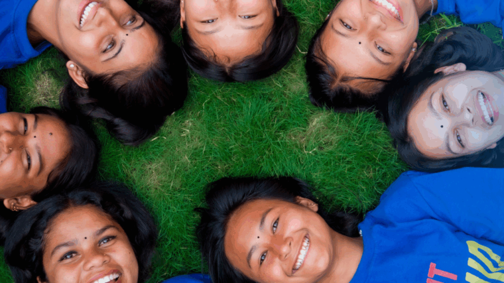 Girls laying on grass in a circle and smiling