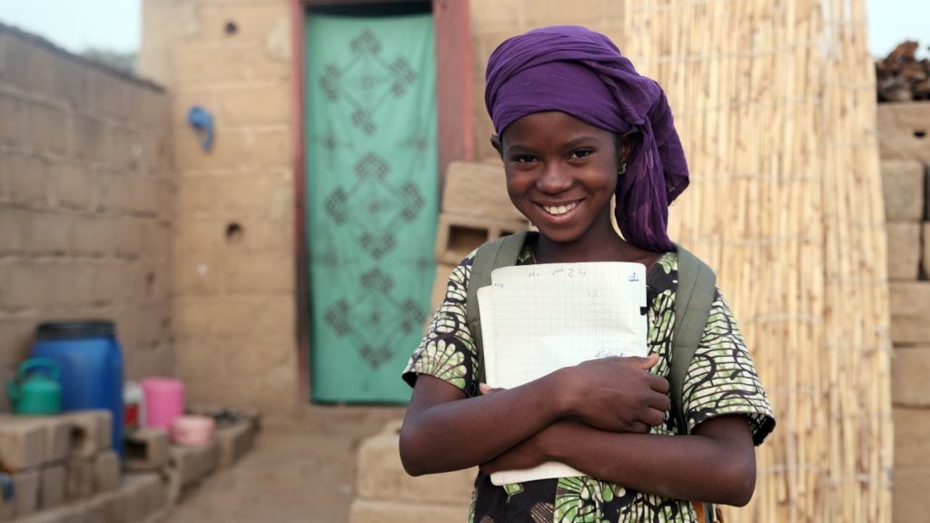 Girl smiling at the camera and holding a notebook