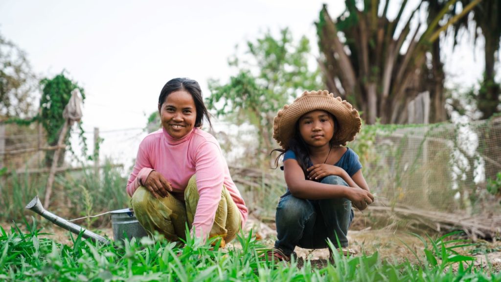 Two people gardening outdoors, smiling and enjoying nature, with plants and greenery in the background.