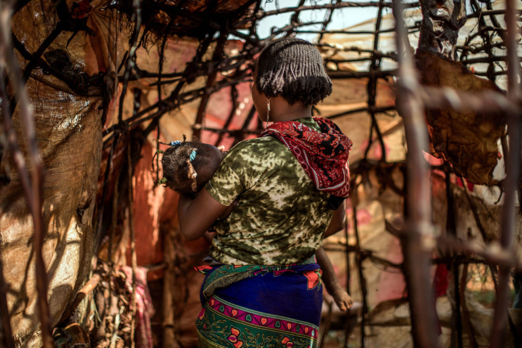 Mother holding child indoors, rustic setting, colorful clothing.