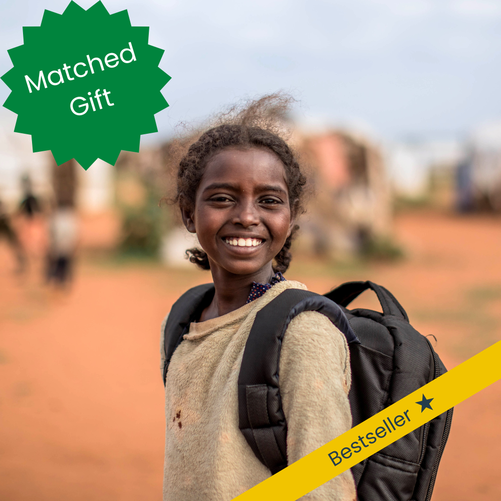 A girl from Sudan in a backpack smiles as she goes to school