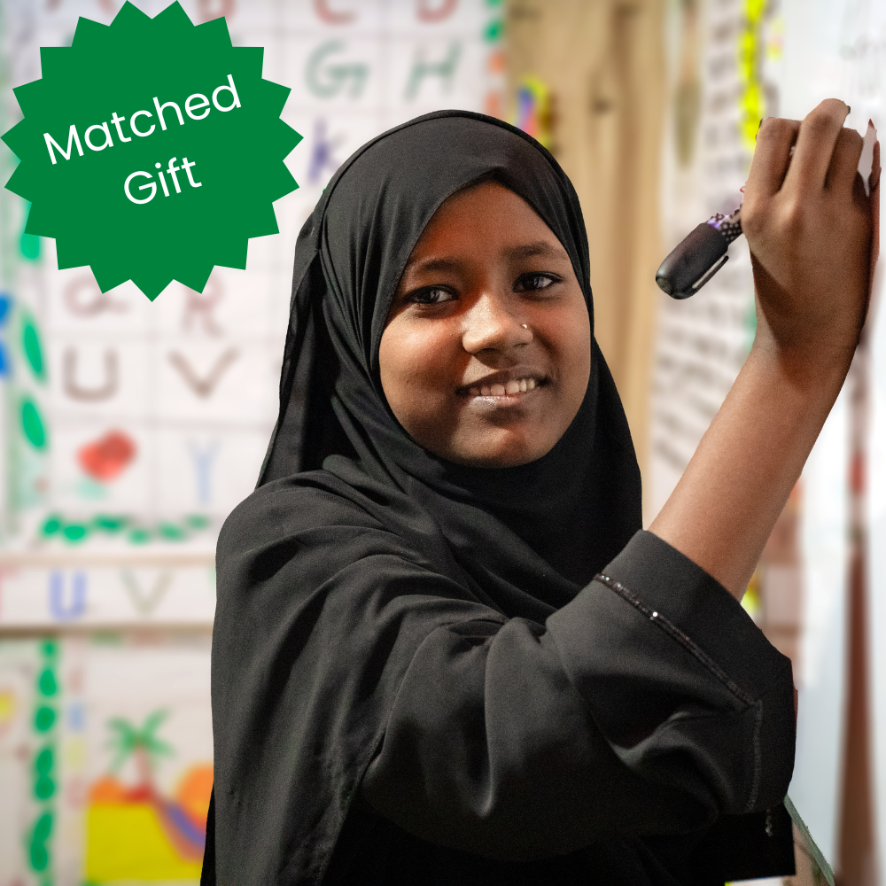 Smiling student writes on whiteboard, promoting matched gift donation campaign.