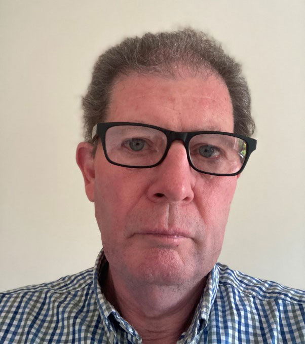 Man wearing glasses and a plaid shirt, standing against a plain background.