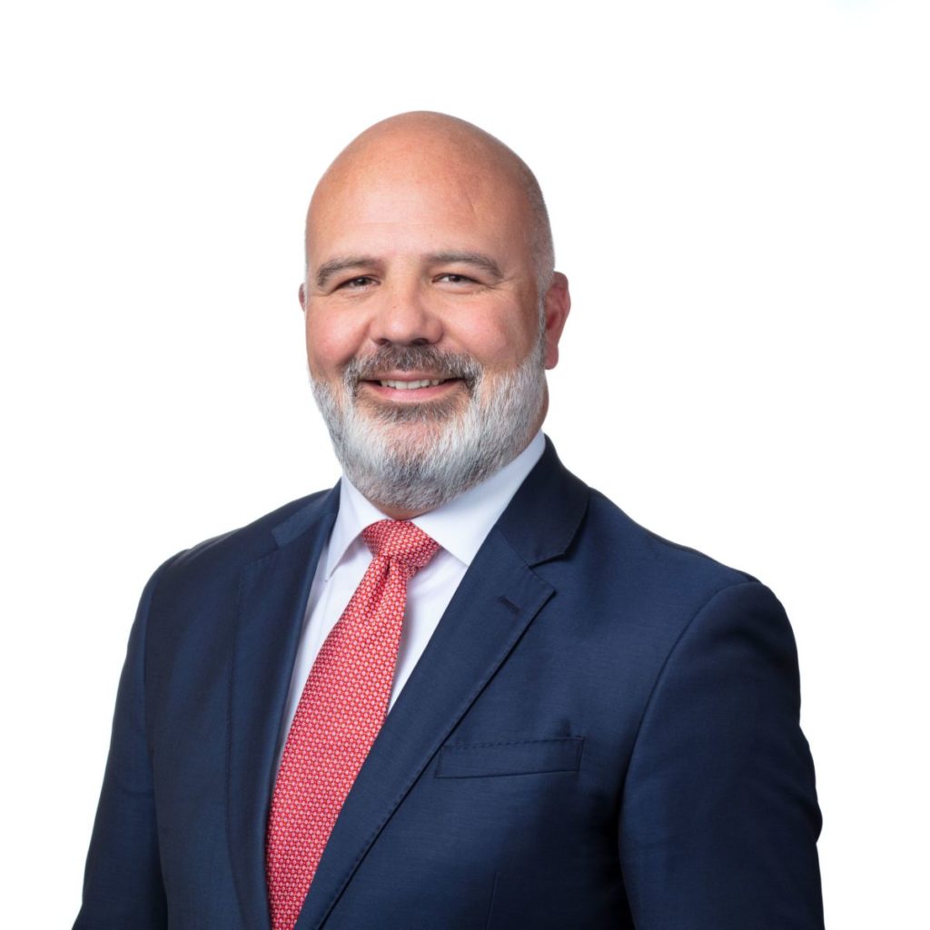 Smiling man in a suit and red tie against a white background, professional portrait.
