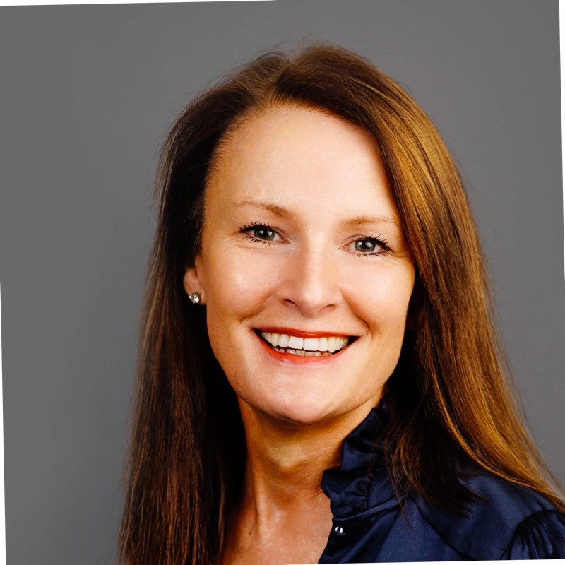 Smiling woman with long brown hair in a navy blouse on a gray background.