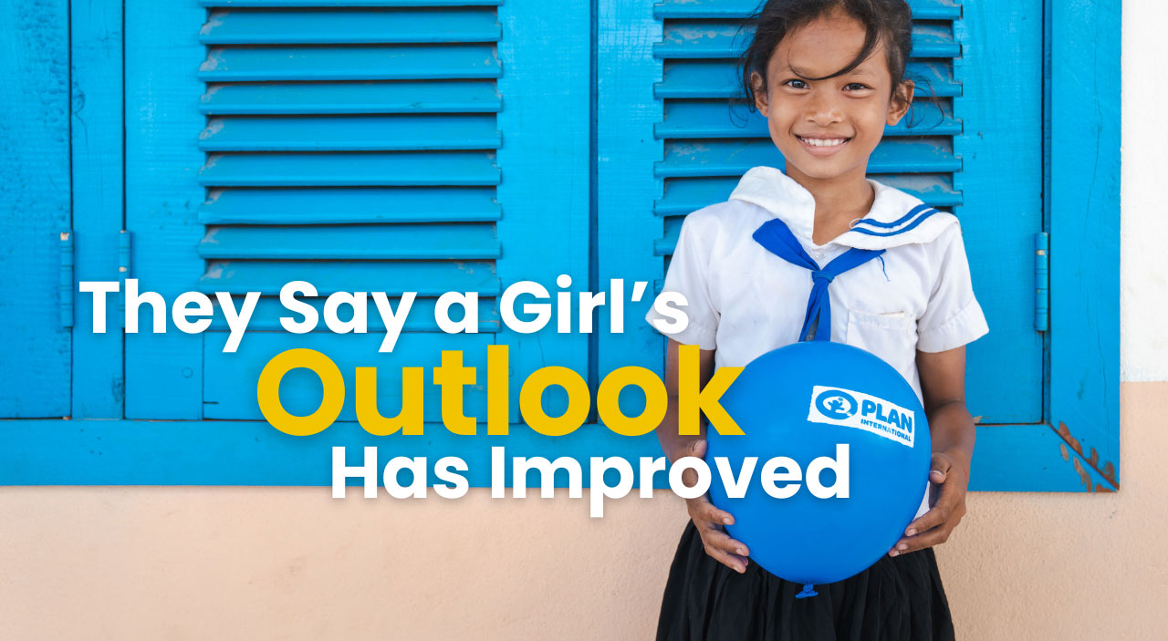Smiling girl holds Plan International balloon, with text: They Say a Girl’s Outlook Has Improved on blue background.