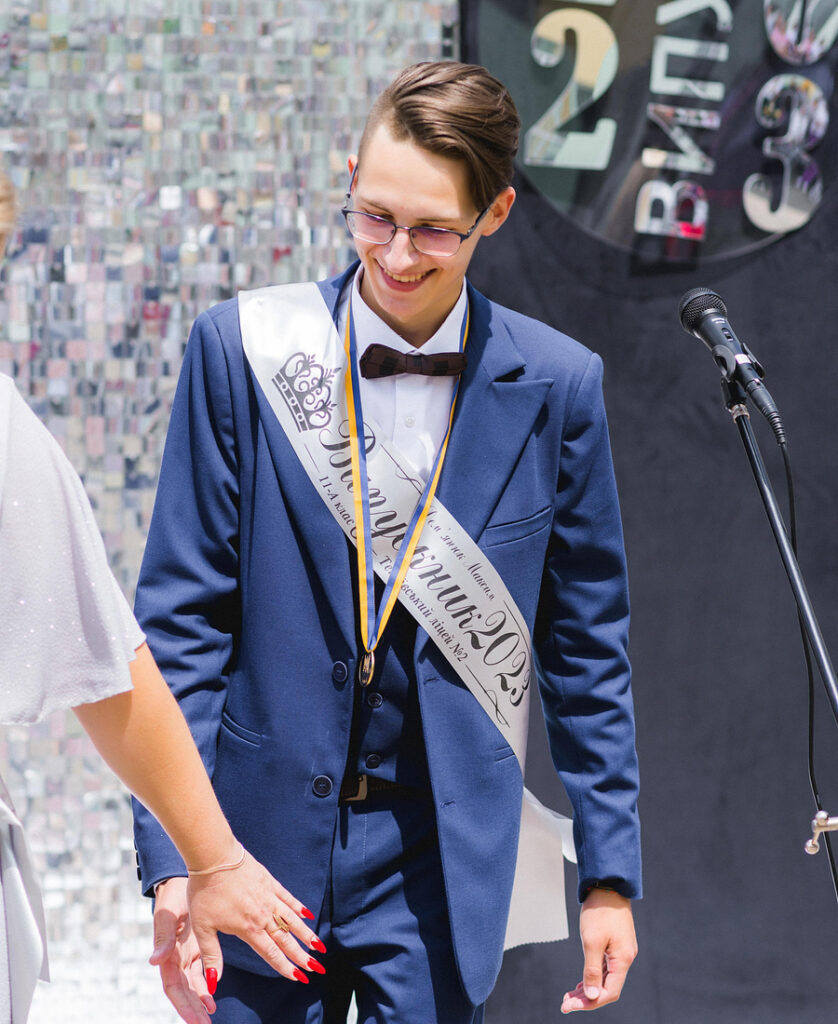 A young man in a blue suit wearing a sash for a graduation ceremony