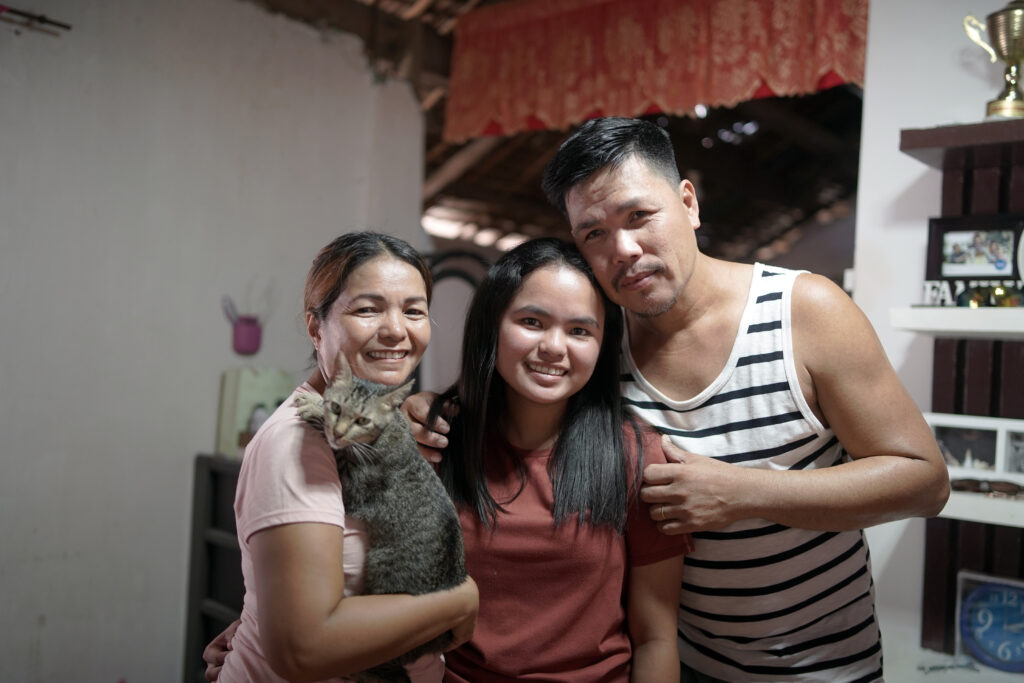 A mother and father hug their daughter and the family cat